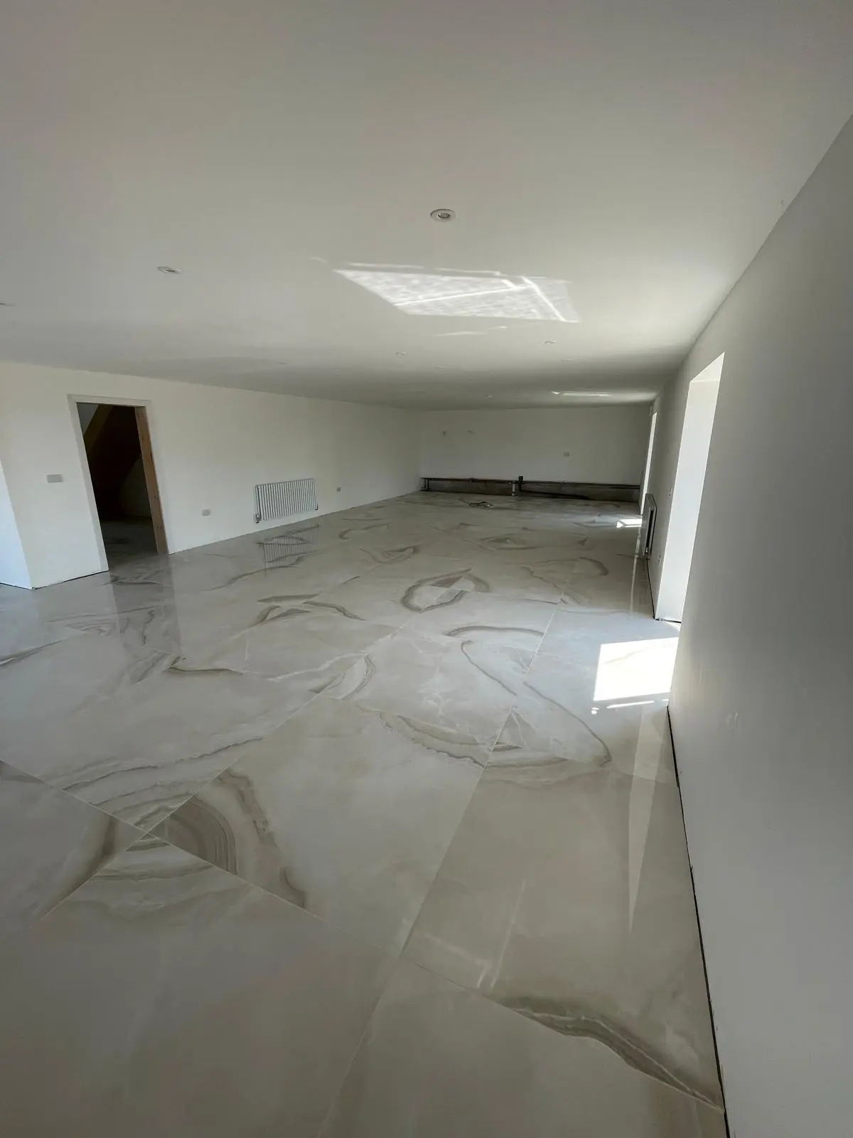 Modern refurbished kitchen with green cabinets, wood wall units, double black oven, tiled flooring, and bright recessed lighting in a spacious open-plan layout.
